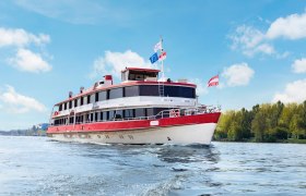 DDSG Blue Danube Schiffahrt, MS Wach, © DDSG Blue Danube/Jakwerth Ein Passagierschiff mit roten und weißen Farben fährt auf einem Fluss unter blauem Himmel.