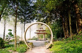 Jardin oriental c Stift Melk Foto Brigitte Kobler Pimiskern, © Stift Melk, B.Kobler-Pimiskern Ein orientalischer Garten mit einem runden Torbogen und einer Pagode im Hintergrund, umgeben von Bäumen und Pflanzen.