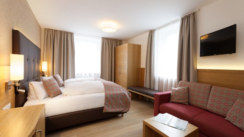 Zimmer im Hotel Donauhof, © Marcella Wallner Modernes Hotelzimmer mit Doppelbett, Sofa, Schrank und Fernseher.