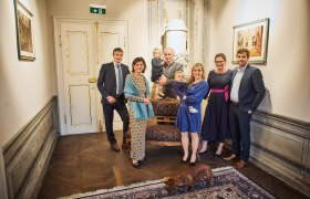 Familie Pichler, © Familie Pichler Eine Gruppe von Menschen posiert in einem eleganten Raum mit einem Hund im Vordergrund.