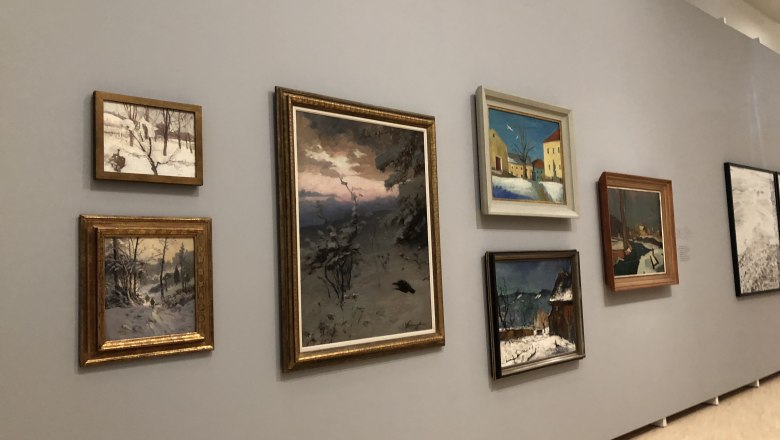 A wall in a gallery with several paintings showing winter landscapes.