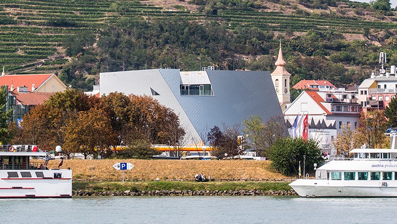 Modern architecture of the Landesgalerie Nieder&ouml;sterreich on the riverbank with surrounding buildings and boats.