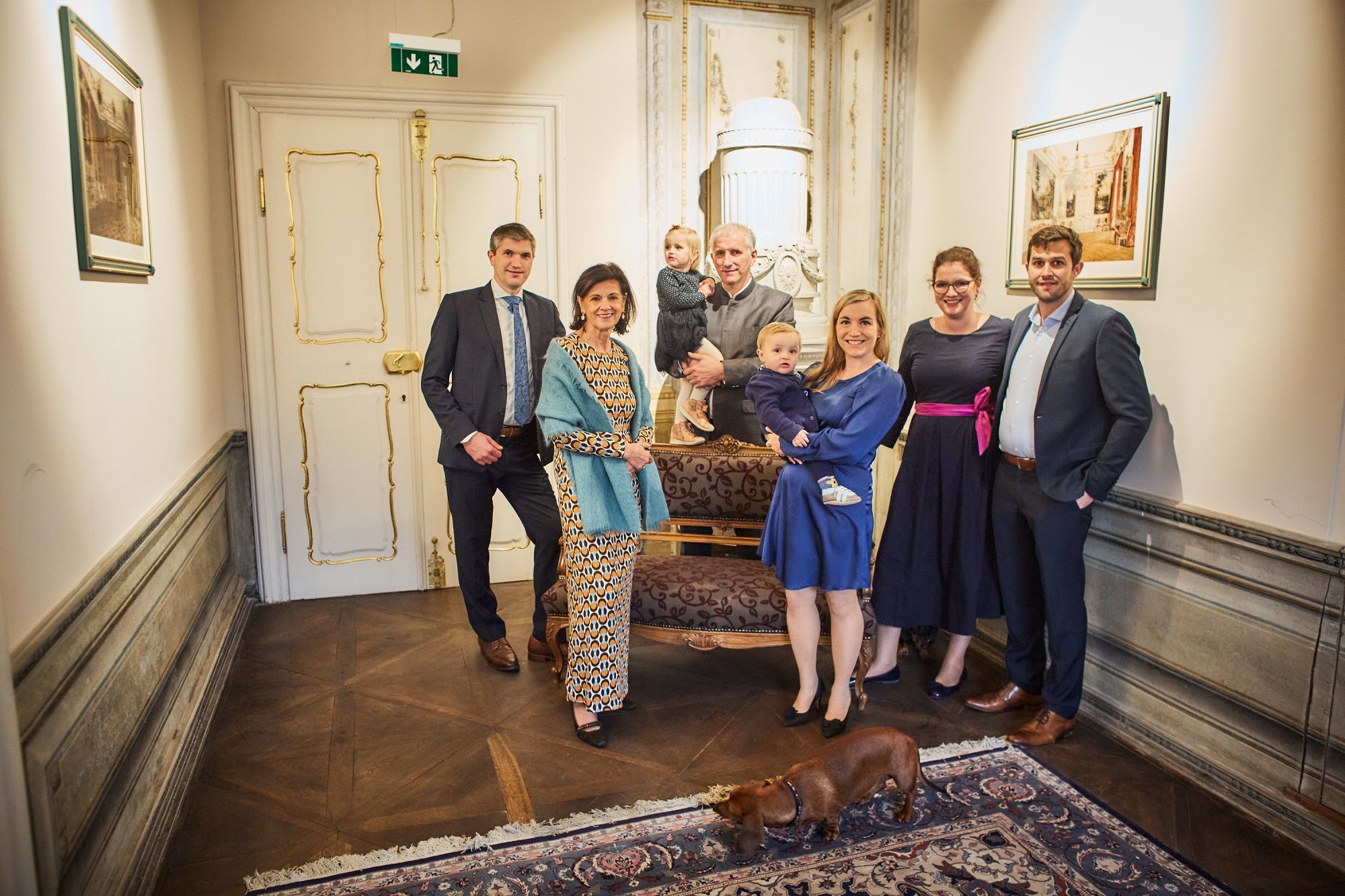 Eine Gruppe von Menschen posiert in einem eleganten Raum mit einem Hund im Vordergrund.