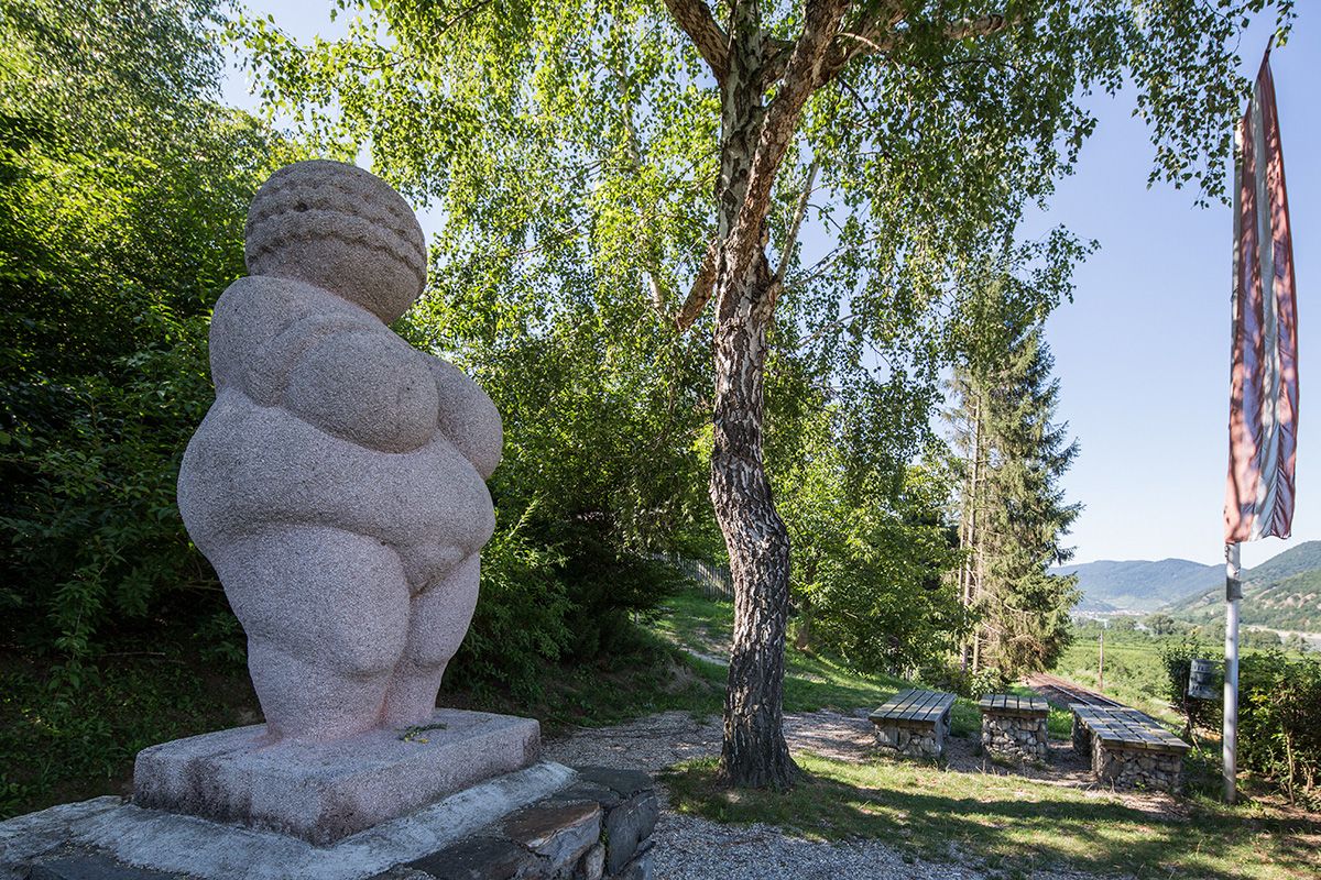 Venus auf einem Sockel im Hintergrund Baum und Bänke