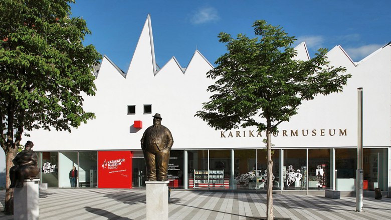 Au&szlig;enansicht des Karikaturmuseums Krems mit Statuen und B&auml;umen.