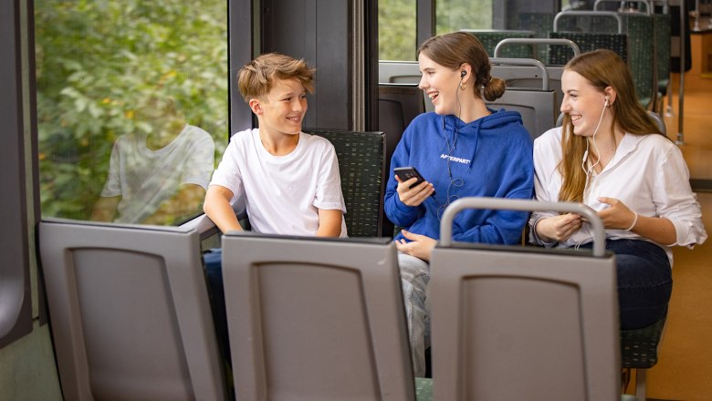 Bursche und 2 Mädchen im Zug. Die Mädchen haben Mobiltelefone in der Hand und Kopfhöhrer im Ohr.