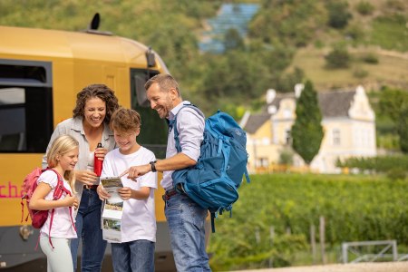 Elternpaar und 1 Bub und 1 Mädchen studieren eine Karte der Wachau. Im Hintergrund ist die Wachaubahn zu sehen.