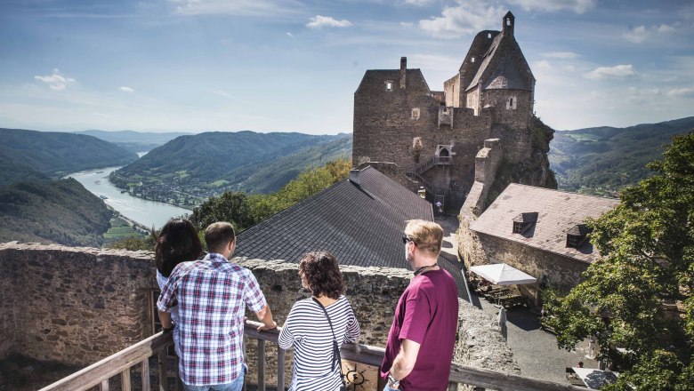 Menschen auf einer Burg mit Blick auf Fluss und Berge.
