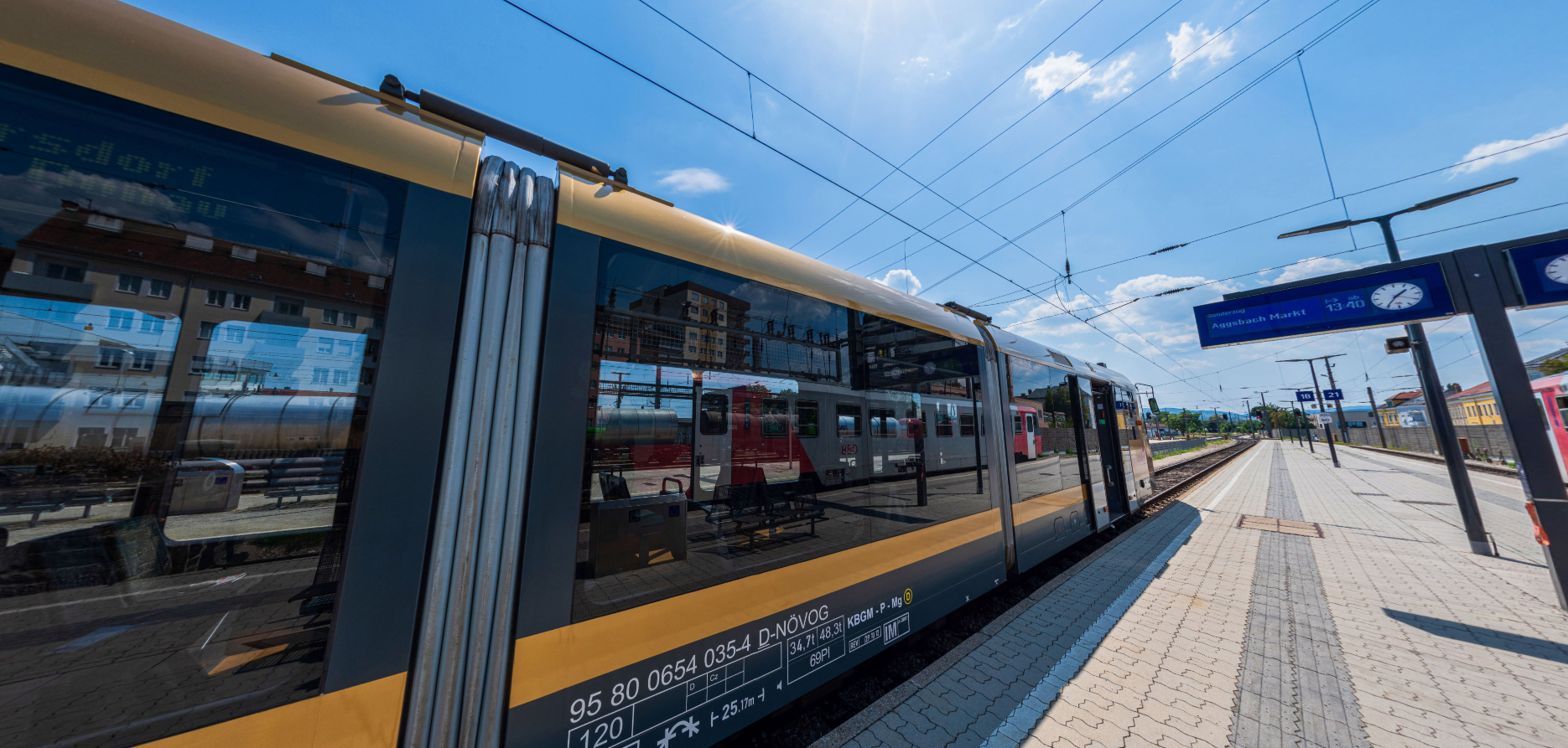 Die goldene Wachaubahn steht am Bahnsteig in Krems. In den Fenstern  spiegeln sich weitere Züge und Gebäude.