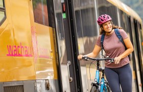 Frau steht mit ihrem Rad neben dem goldenen Triebwagen der Wachaubahn