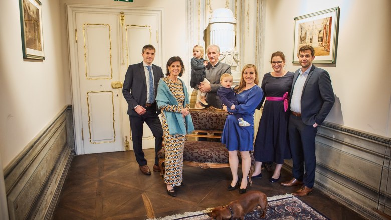 A group of people pose in an elegant room with a dog in the foreground.