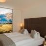 Modernes Hotelzimmer mit Doppelbett, dekorativen Kissen und großem Landschaftsbild an der Wand.