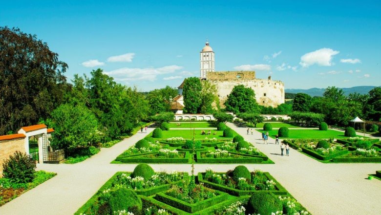 Vorne ein kunstvoll angelegter Garten mit Buchsornamenten und Pflanzenvielfalt, dahinter das eindrucksvolle Renaissanceschloss Schallaburg.