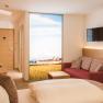 Modernes Hotelzimmer mit Doppelbett, rotem Sofa, Flachbildfernseher und großem Fenster mit Landschaftsausblick.