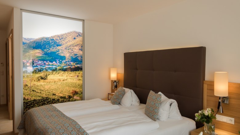Modernes Hotelzimmer mit Doppelbett, dekorativen Kissen und großem Landschaftsbild an der Wand.