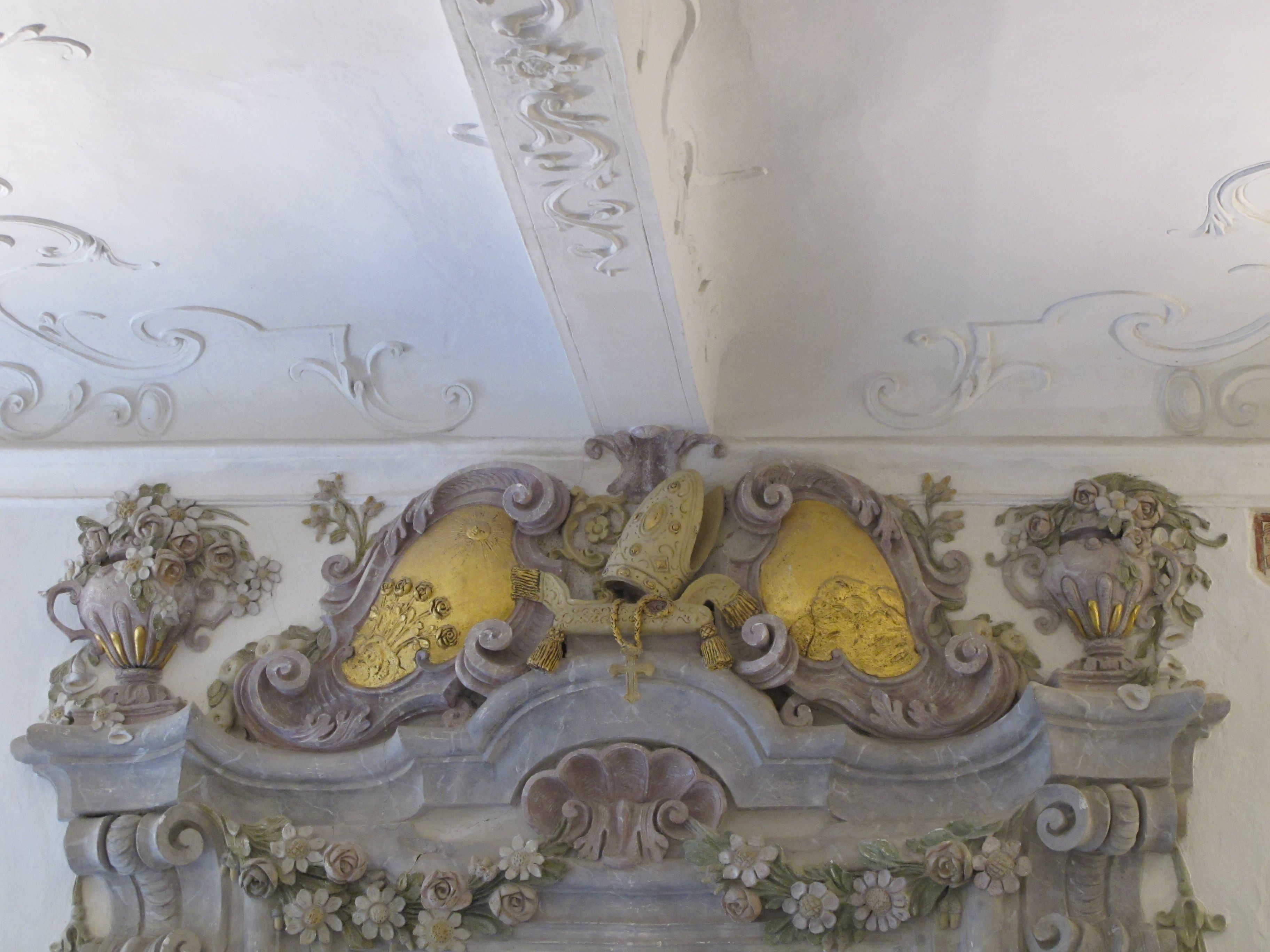 Barocke Stuckverzierung mit floralen Motiven und goldenen Elementen an einer Decke.