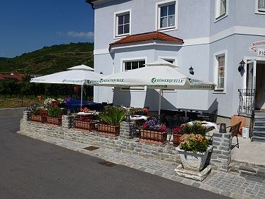 Au&szlig;enansicht eines Geb&auml;udes mit Terrasse und Sonnenschirmen.