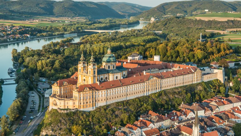 Luftaufnahme des Stifts Melk in Österreich, umgeben von grüner Landschaft und der Donau.