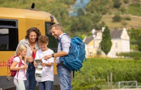 Elternpaar und 1 Bub und 1 Mädchen studieren eine Karte der Wachau. Im Hintergrund ist die Wachaubahn zu sehen.